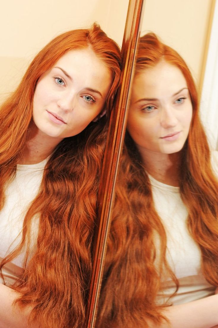 a woman with long red hair is looking at herself in the mirror