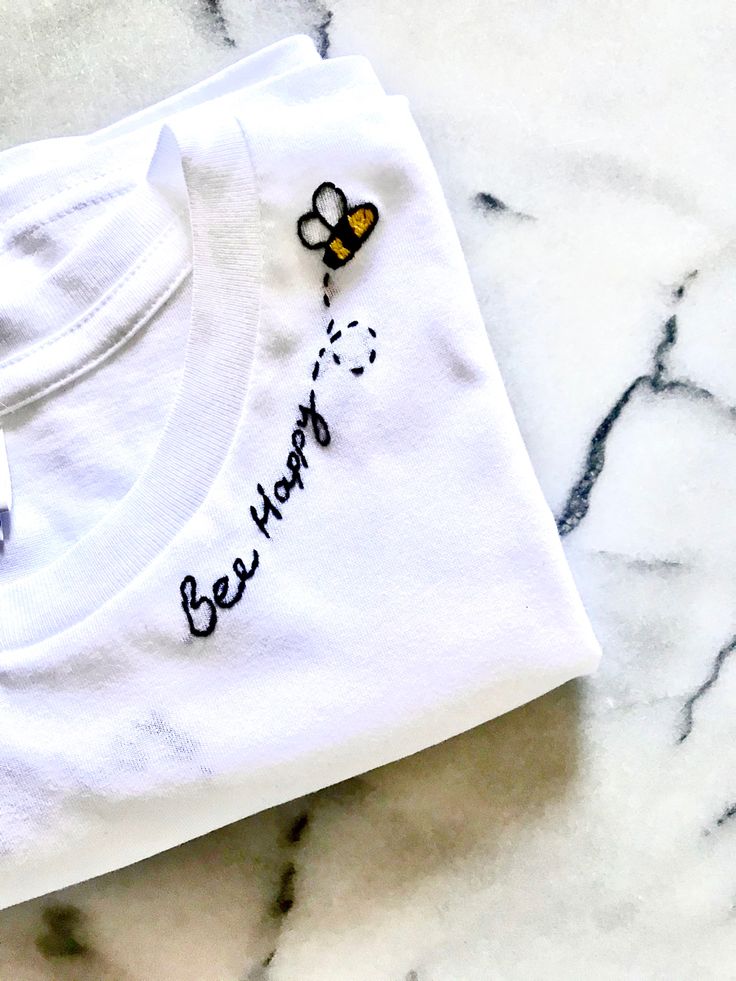 a white t - shirt with a bee embroidered on it