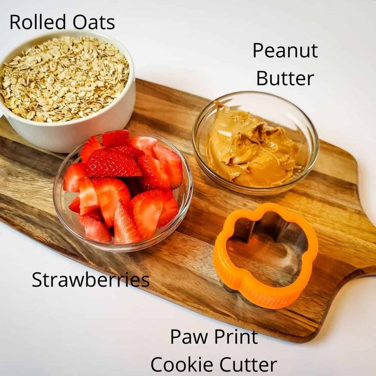 the ingredients to make oatmeal are displayed on a cutting board, including strawberries, peanut butter and raw berries