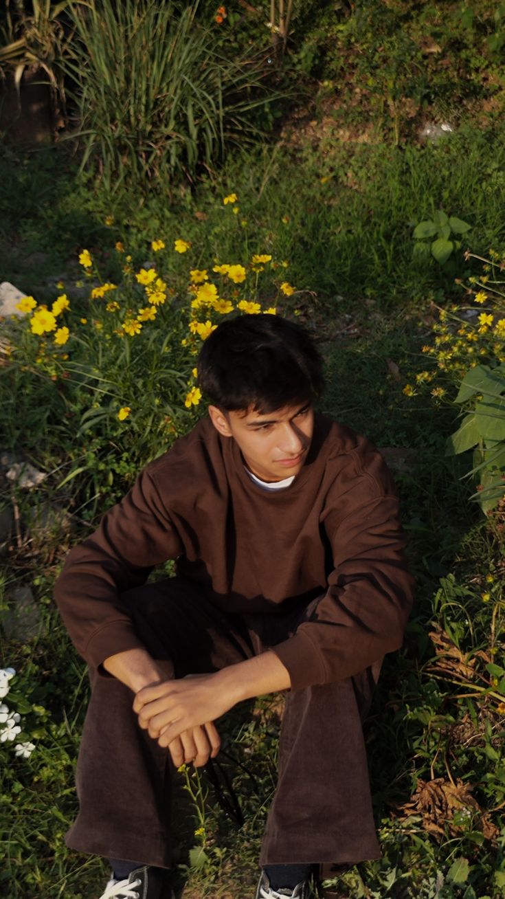 a young man sitting on the ground in front of flowers