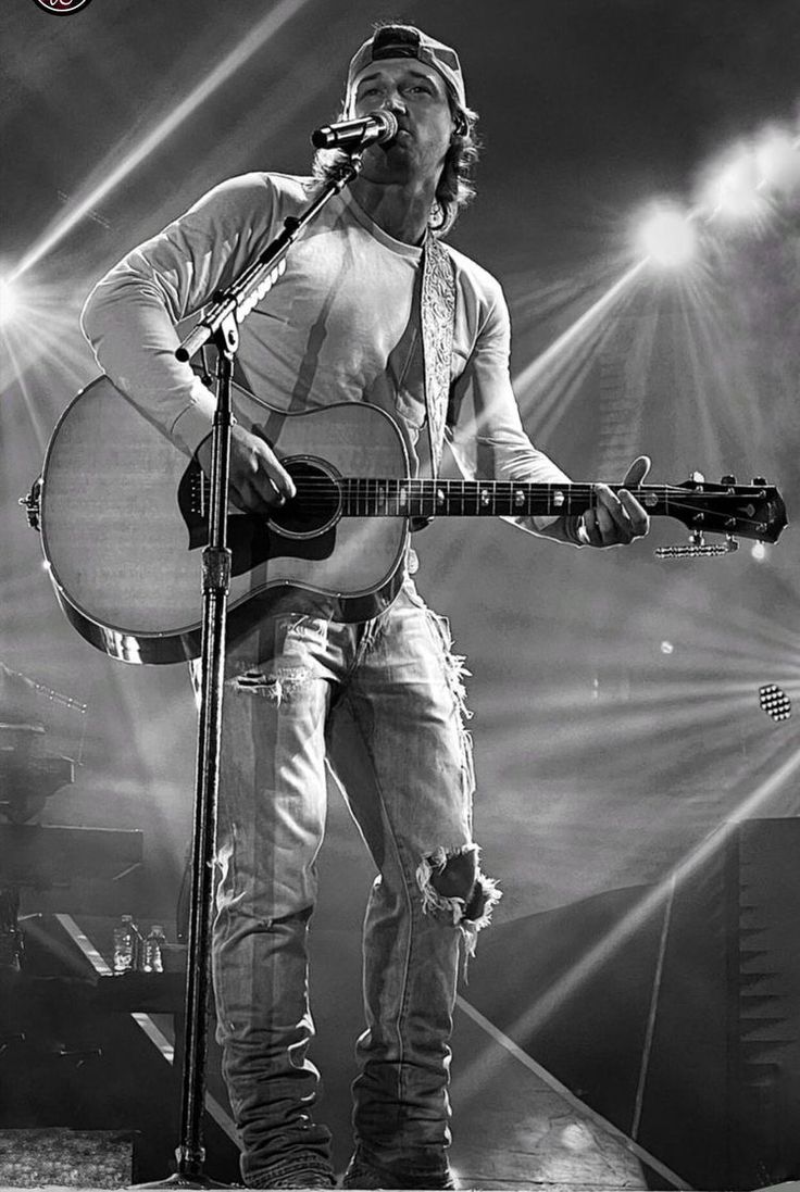 a black and white photo of a man singing into a microphone while holding an acoustic guitar