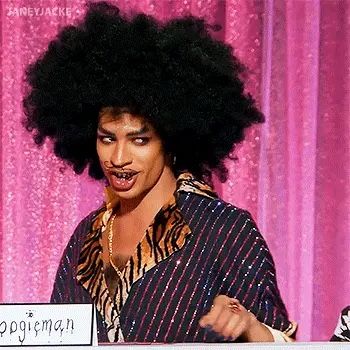 a man with an afro standing in front of a pink curtain and holding a sign