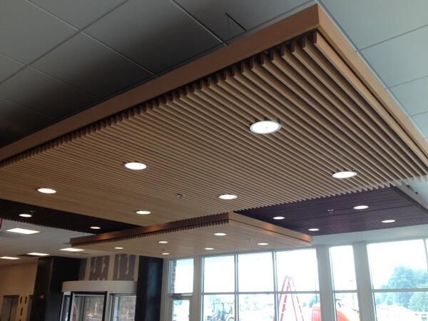 the ceiling is covered with wooden slats and lights in an empty room that also has large windows