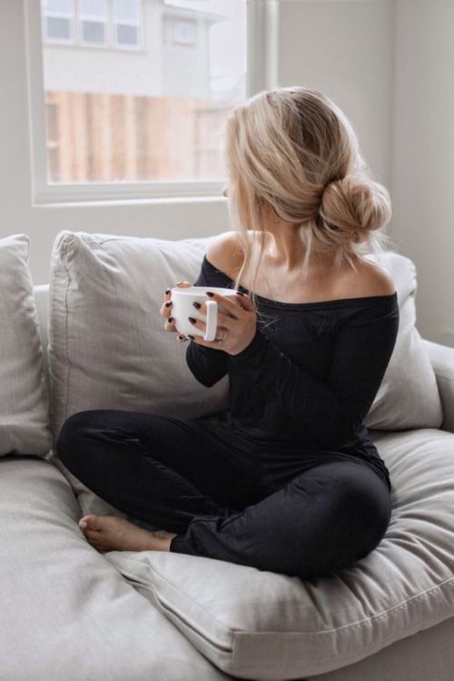 a woman sitting on a couch holding a coffee cup in her hand and looking out the window