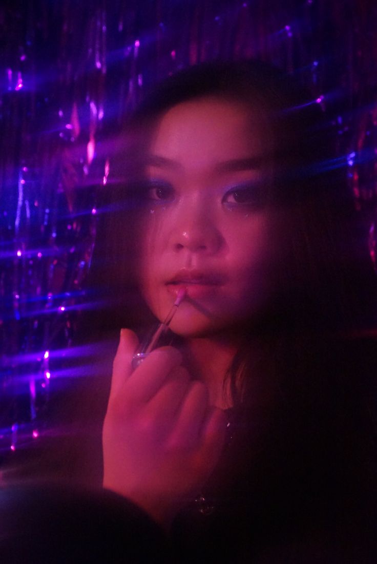 a woman is looking at the camera while she brushes her teeth in front of purple and blue lights