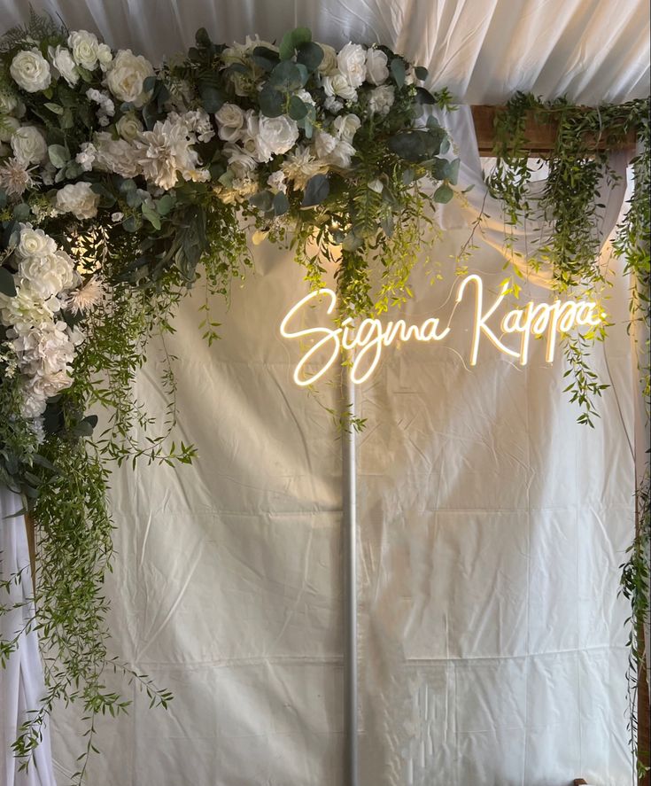 the wedding arch is decorated with white flowers and greenery as well as neon lights