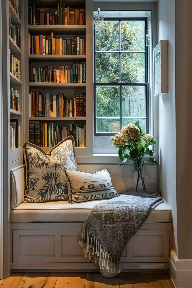 a window seat in front of a book shelf filled with books and flowers on top of it