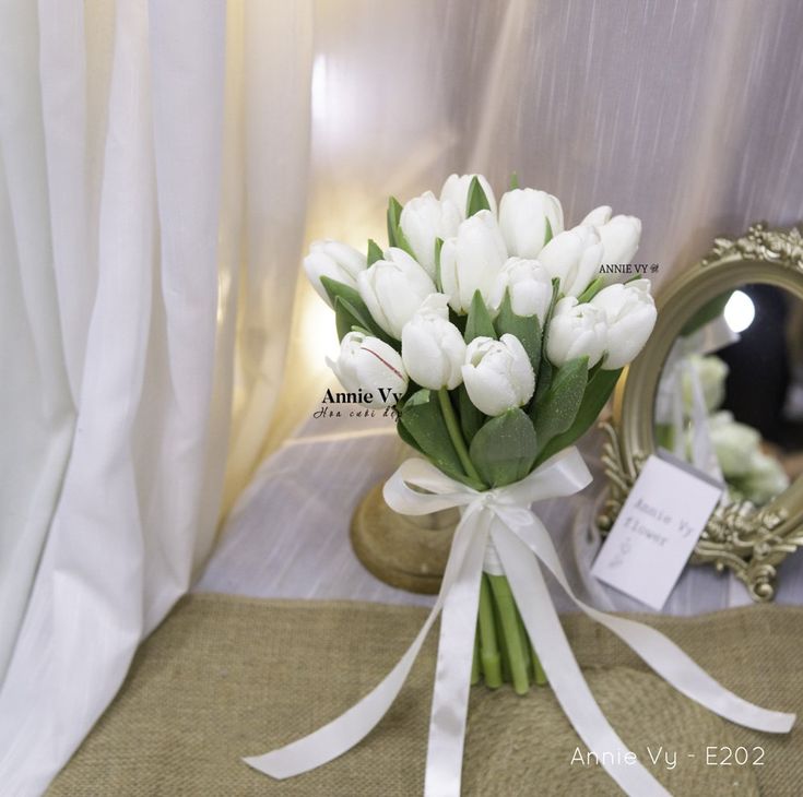 a bouquet of white tulips sits on a table next to a mirror