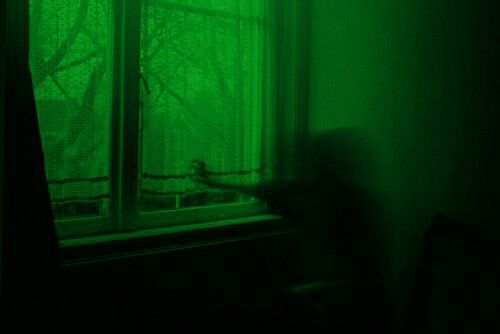 a person standing in front of a window with green light coming through the windowsill