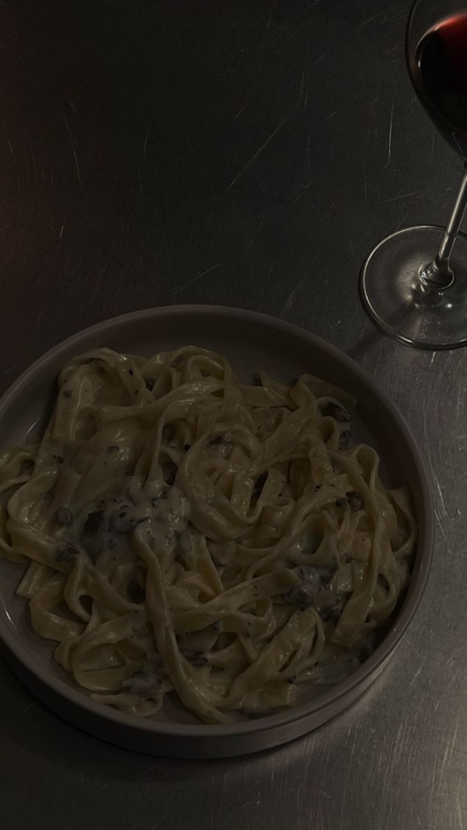 a bowl of pasta next to a glass of red wine on a metal counter top