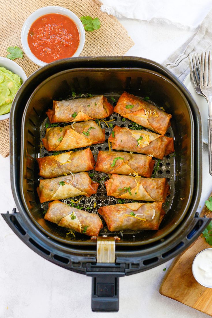 an air fryer filled with meat and vegetable spring rolls next to a bowl of sauce