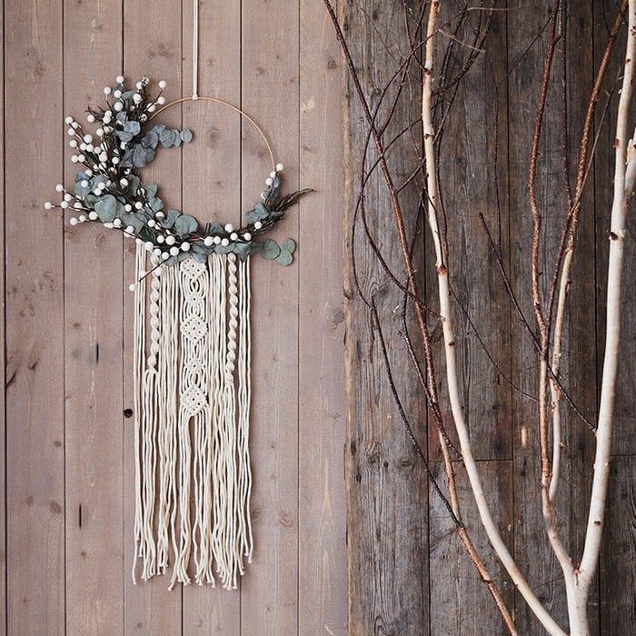 a wall hanging with beads and flowers on it next to a tree branch in front of a wooden fence