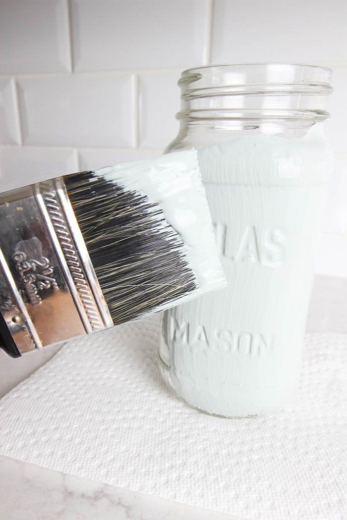 a mason jar filled with white paint sitting on top of a counter next to a brush