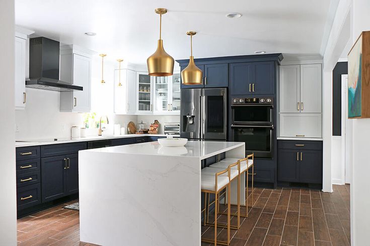 a kitchen with blue cabinets and white counter tops, gold pendant lights over the island