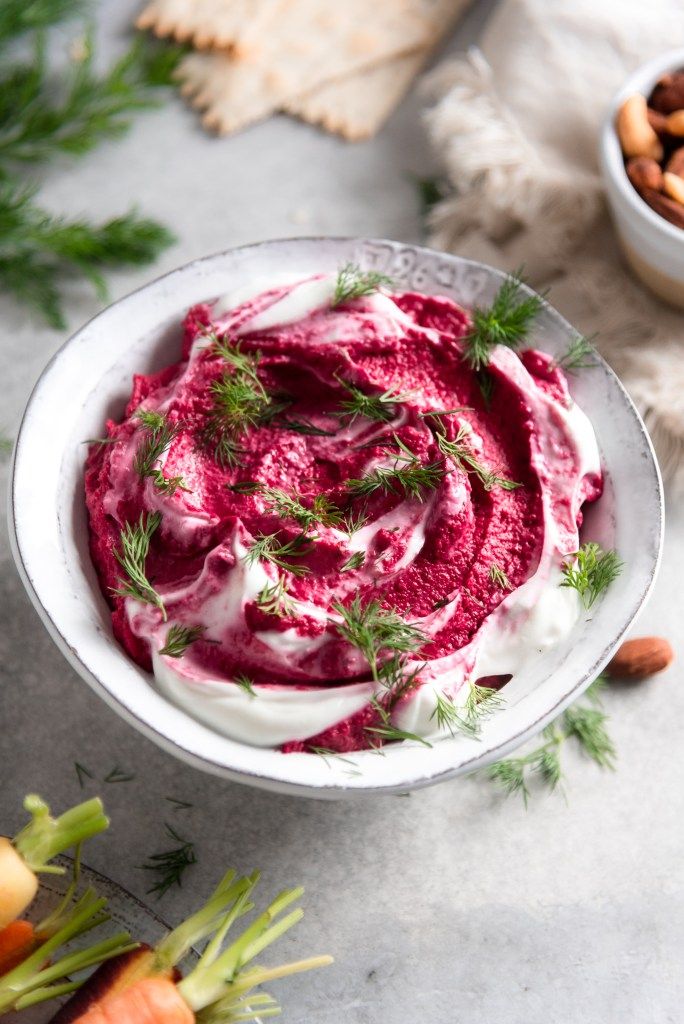 a white bowl filled with beet hummus next to some nuts and carrots