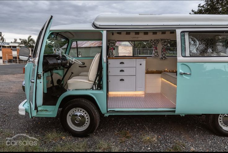 an old blue and white camper van with the door open, parked on gravel