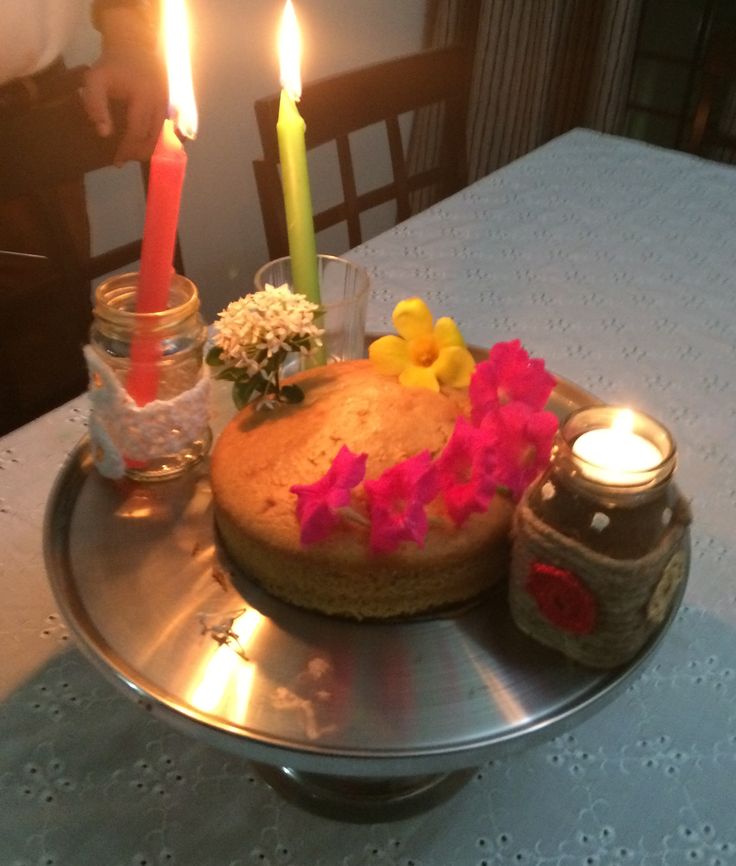 a cake sitting on top of a metal plate covered in flowers and candles next to jars