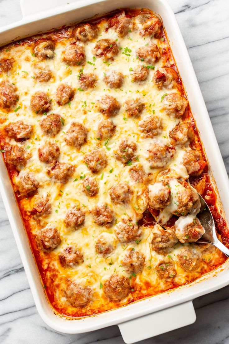 a casserole dish with meatballs and cheese in it on a marble surface