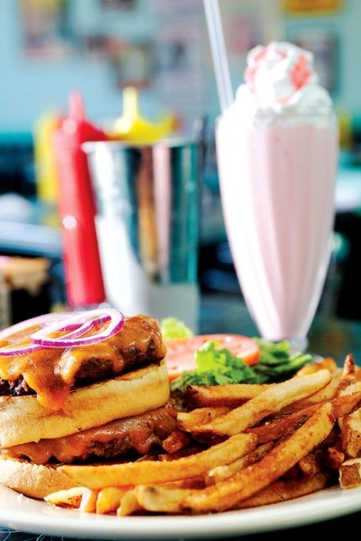 a white plate topped with a sandwich and french fries next to a cup of milkshake