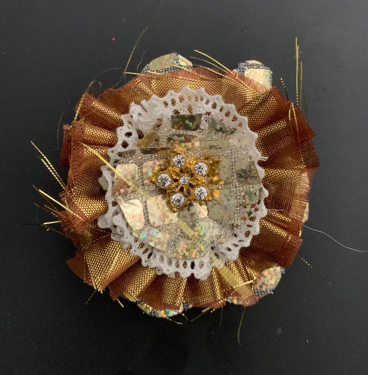 a close up of a brooch on a black surface with gold and white trim