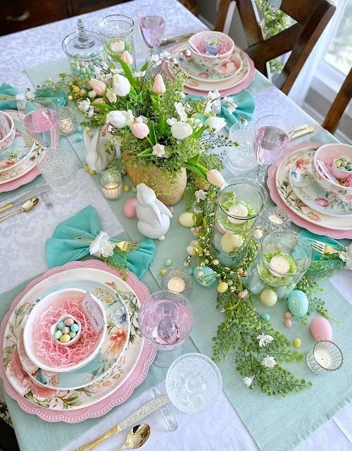 the table is set for easter dinner with pink and green plates, silverware, and flowers