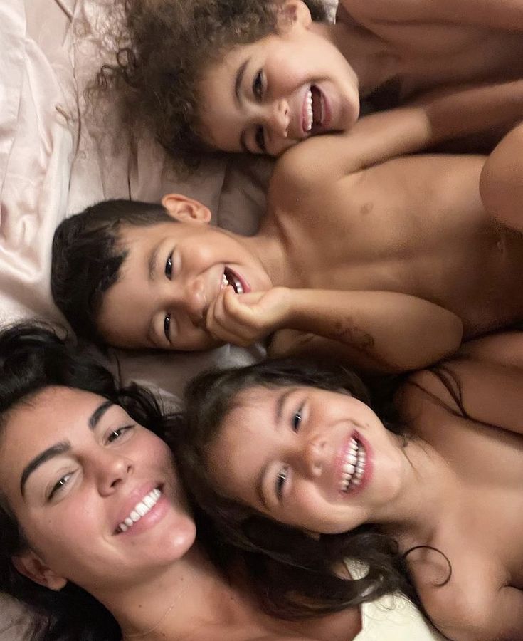 three women and two children are laying on the bed with their mouths open while smiling