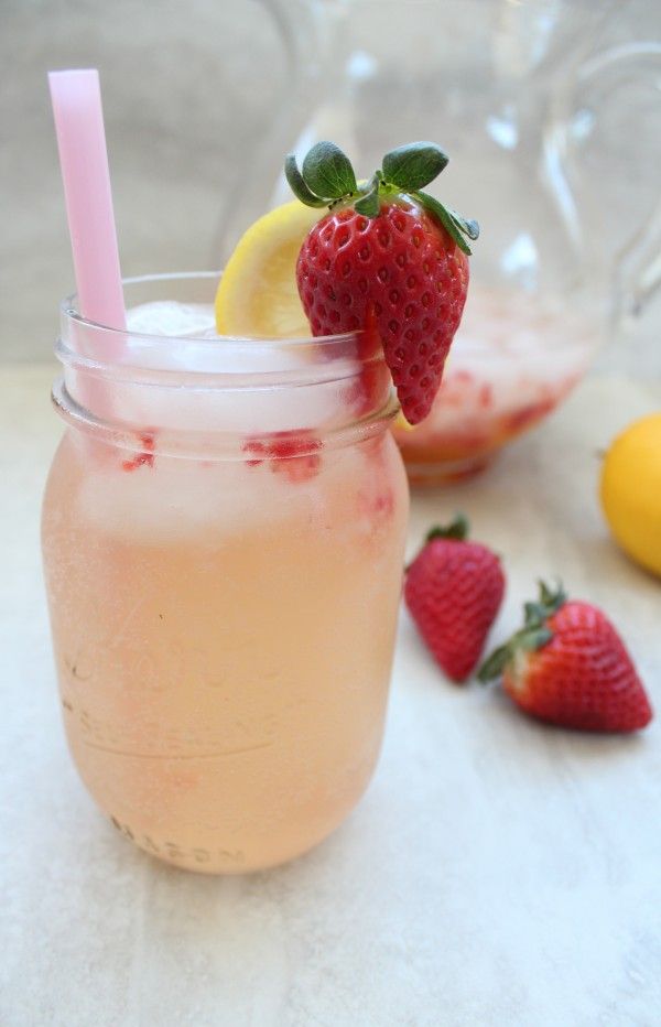 a strawberry lemonade drink in a mason jar with strawberries and lemons around it