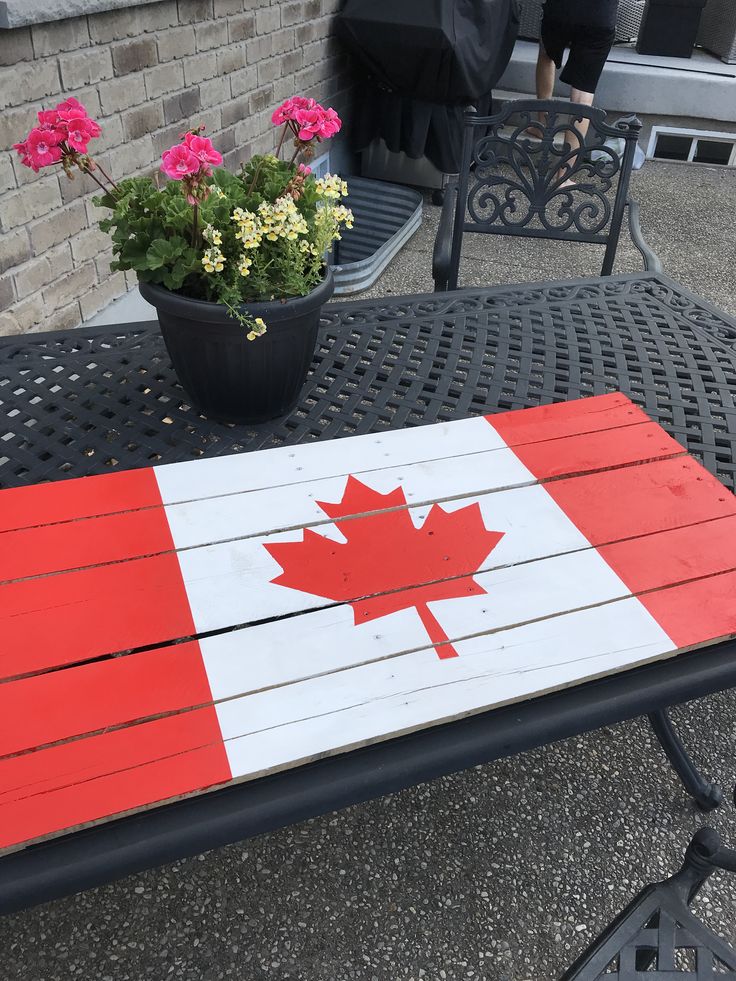 a canadian flag painted on top of a table with potted flowers in the background