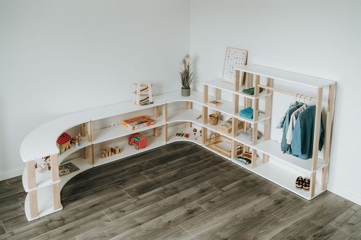 a white curved shelf with books and toys on it next to a wall mounted coat rack