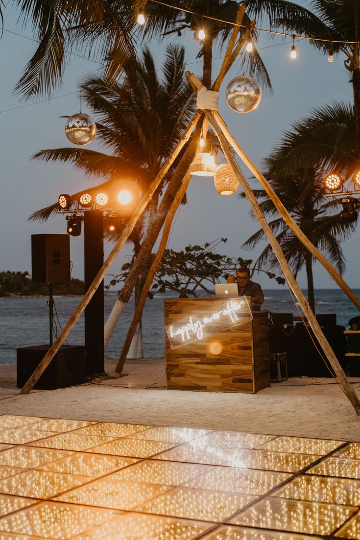 a man sitting at a table in front of some lights and palm trees on the beach