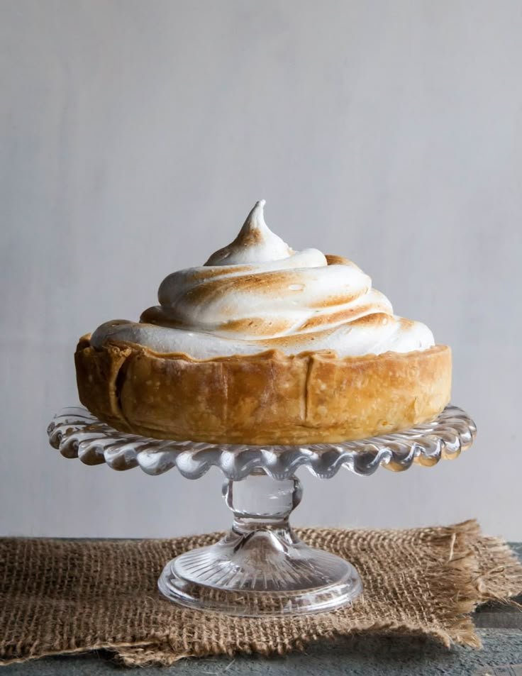 a cake on a glass stand with whipped cream in the top and frosting on top