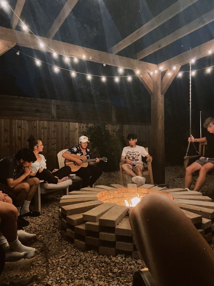 group of people sitting around a fire pit at night with string lights on the roof