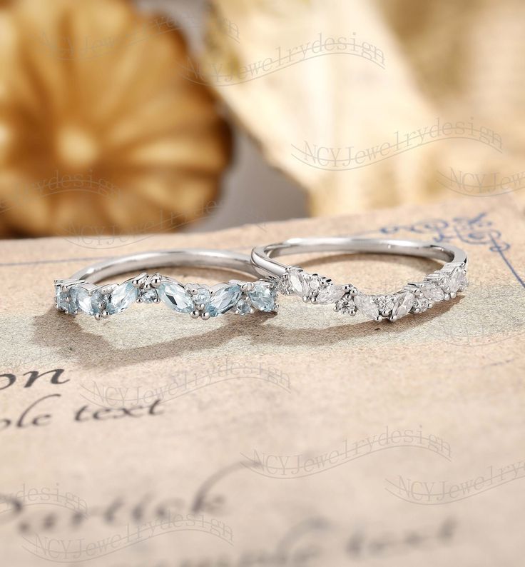 two white gold wedding bands with blue topazte stones on an antique card board