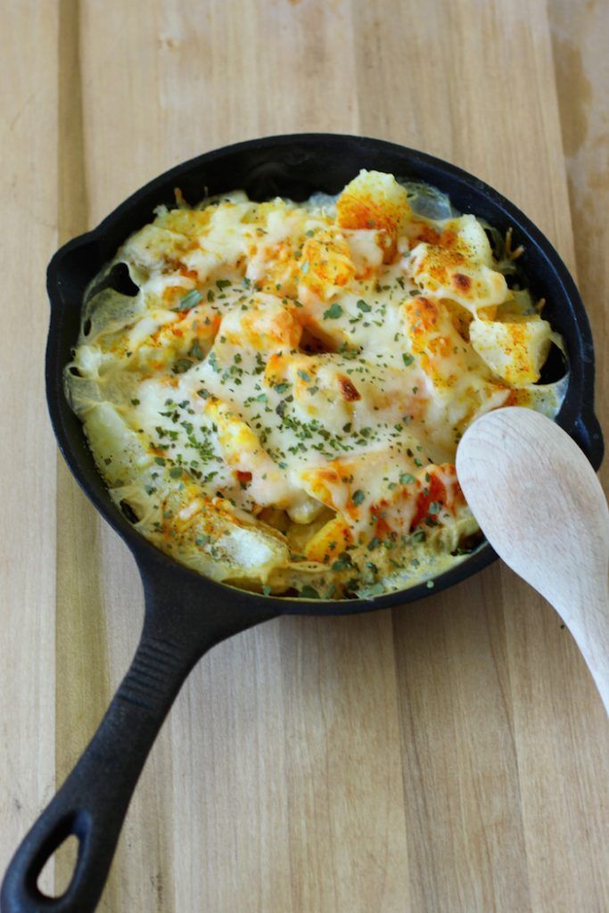 a skillet filled with food on top of a wooden table next to a spoon