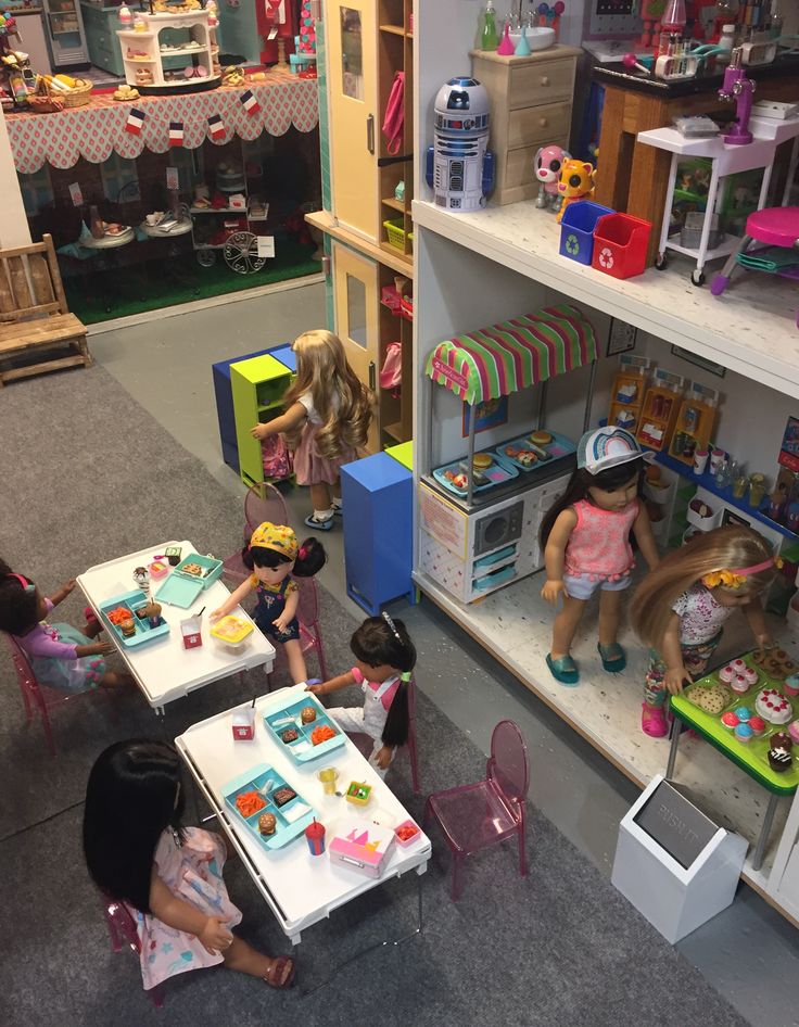 several children are sitting at tables in a playroom with toys on the floor and shelves