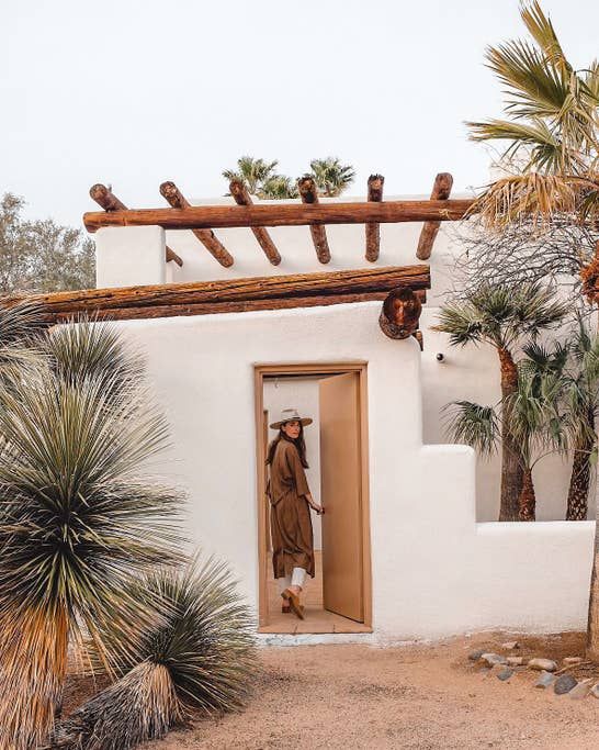 a person standing in an open door to a small white building with palm trees around it