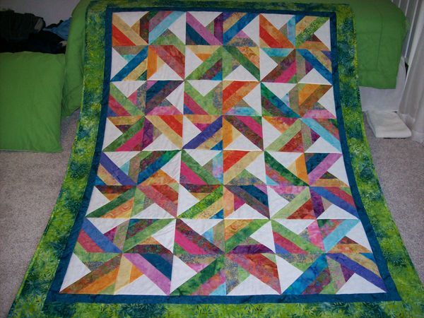 a colorful quilt is laying on the floor in front of a green pillow and pillows