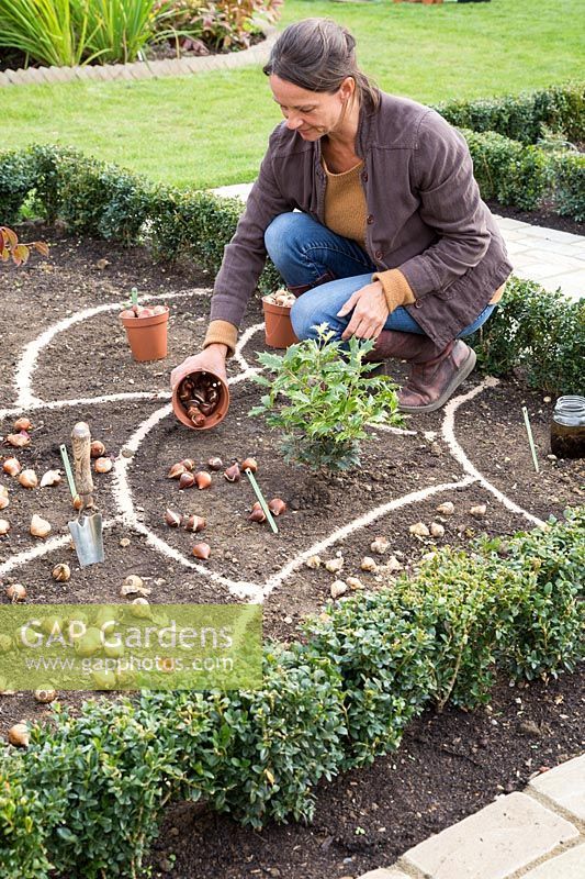 a woman kneeling down in the middle of a garden with plants growing out of it