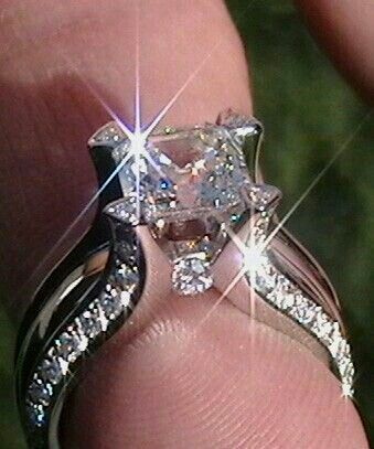 a person's hand holding an engagement ring with two diamonds on top of it