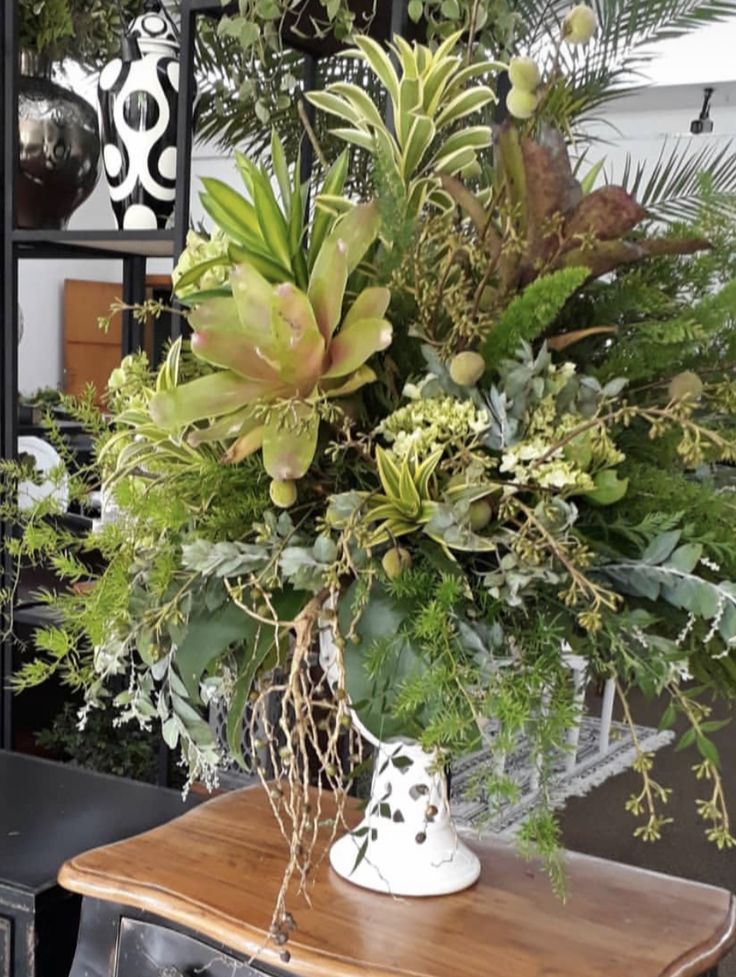 a vase filled with green plants on top of a wooden table