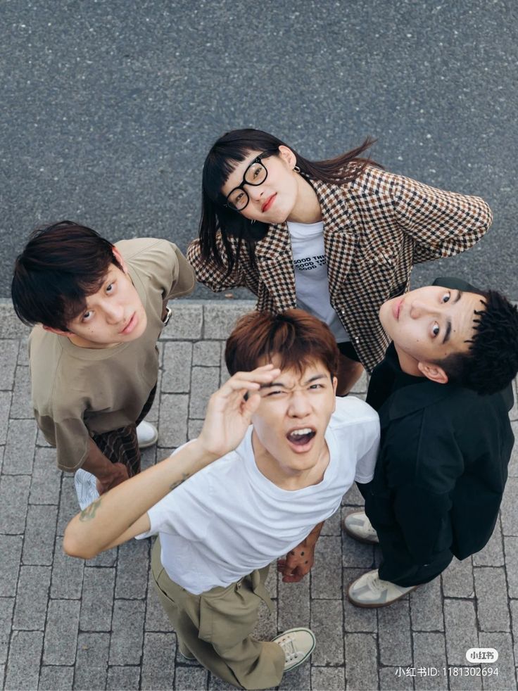 four people standing on the ground with one holding his hand up to his ear and looking at the camera