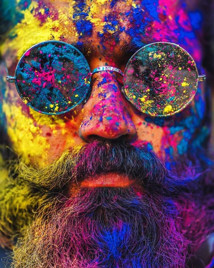 a man with glasses and beard covered in colored paint is looking at the camera while he's wearing sunglasses