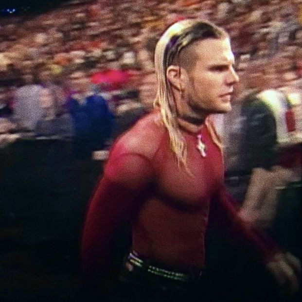 a man with long hair and no shirt is walking in front of an audience at a sporting event