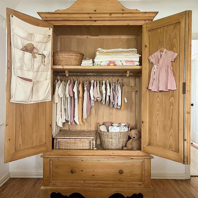 an open wooden closet with clothes and baskets