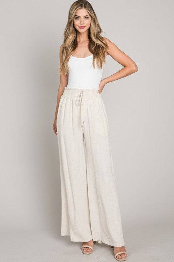 Embrace comfort and style with our Soft Linen Smocked Waist Wide Leg Pants, perfect for your resort collection. Designed with an elastic waistband, these pants ensure all-day comfort and a flexible fit. The wide-leg design adds a touch of elegance and creates a flowing silhouette, ideal for any casual or upscale event. Available in versatile Black and Natural colors, these trousers are a superb choice for those seeking both style and convenience. Constructed from a blend of 60% cotton and 40% linen, these pants are travel-friendly with easy care instructions and reduced wrinkling. Offered in sizes Small, Medium, and Large, they are designed to cater to a variety of body types, ensuring a great fit for every wearer. Ideal for lounging in luxury or stepping out in style, these wide-leg trous White Bottoms With Gathered Waist For Summer, Summer Vacation Bottoms With Pull-on Style, White Smocked Back Bottoms For Summer, Spring Vacation Bottoms With Smocked Back, Summer Vacation Wide Leg Full Length Pants, Vacation Wide Leg Pants With Elastic Waistband, Casual Wide Leg Pants For Beach, Summer Beach Bottoms With Pull-on Style, Summer Vacation Bottoms With Gathered Waist