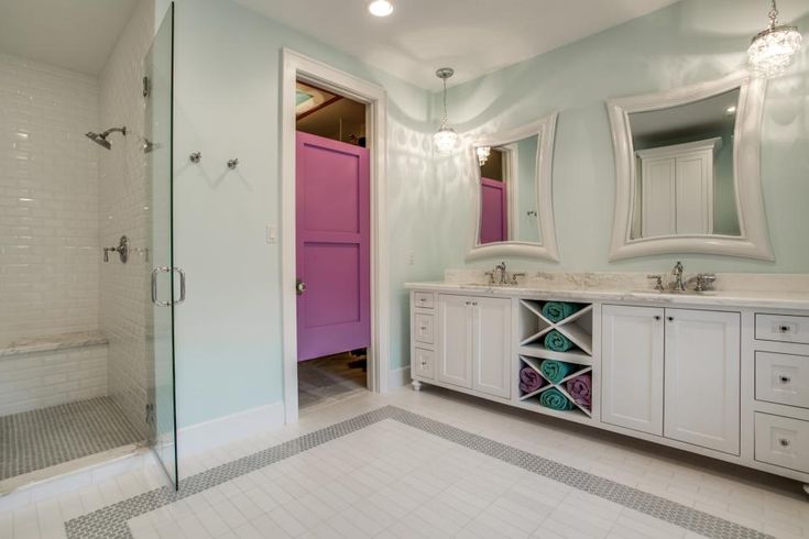 a white bathroom with two sinks and a pink door in the shower area is shown