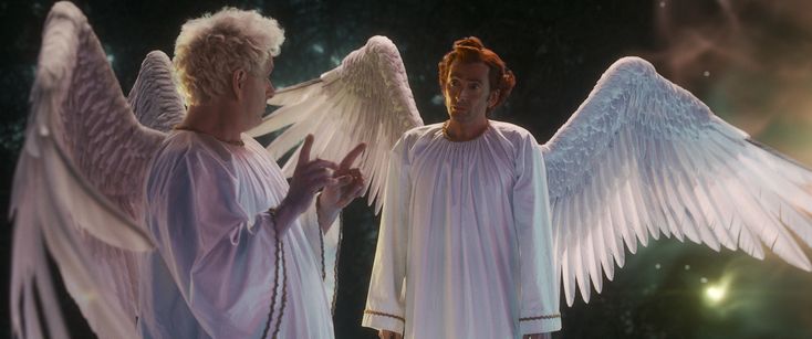 two people dressed in white with angel wings on their shoulders, one pointing at the other