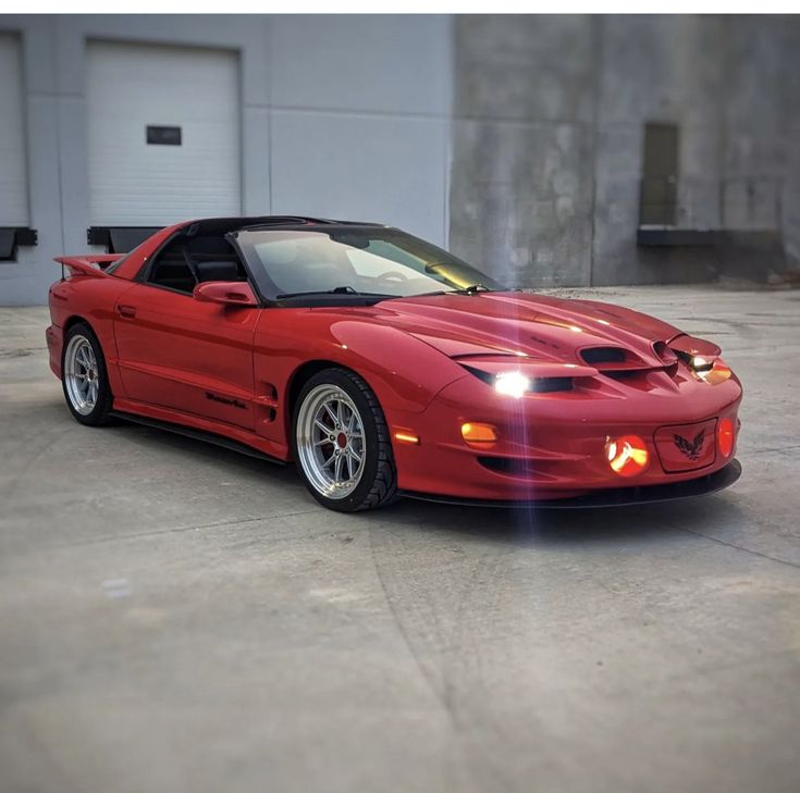 a red sports car is parked in front of a garage with its hood up and lights on