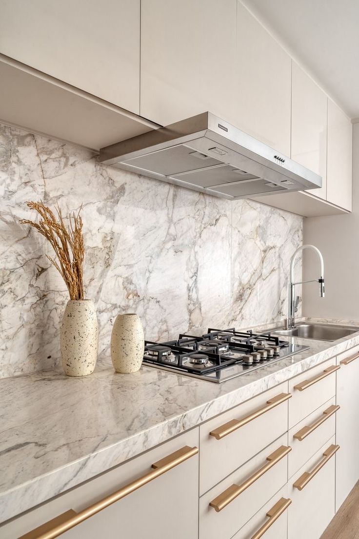 a kitchen with marble counter tops and gold trimming on the cabinets, along with two vases filled with flowers