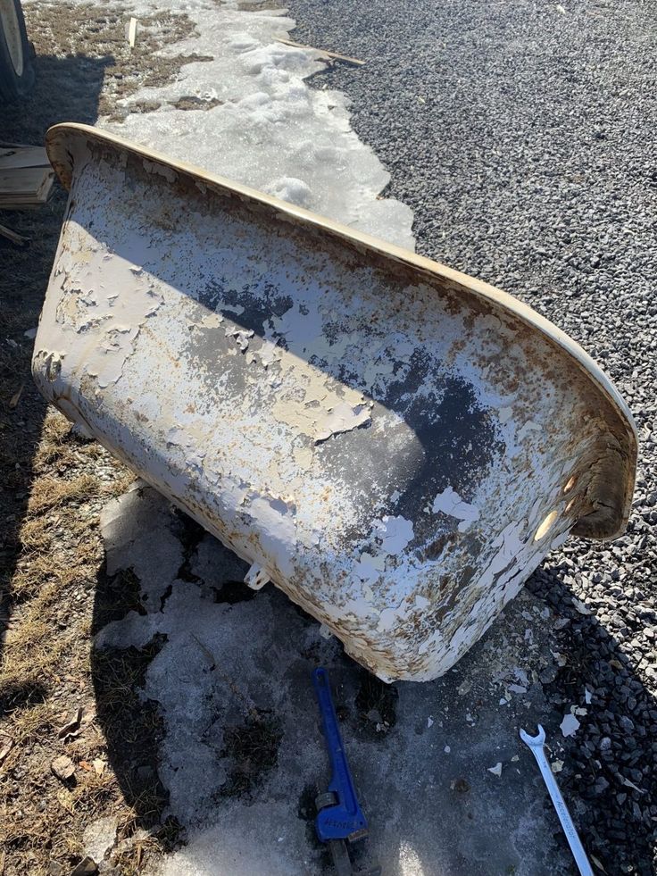 an old bathtub sitting on the side of a road next to a blue wrench